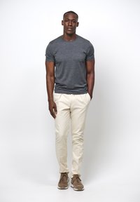 Grå crew-neck t-shirt, beige skräddarsydda byxor och bruna sneakers. Släta texturer med en åtsittande design och subtila färgkontraster.