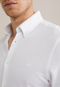 Fehér, texturált anyagú gombos ing, klasszikus gallérral, kisméretű logóval a mellrészen és gyöngyházfényű gombokkal.