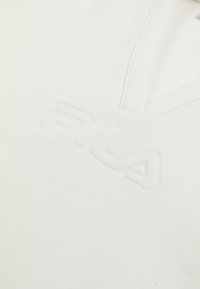 Biała koszulka z dekoltem w serek, z delikatnie przeszytym logo FILA na piersi, podkreślająca minimalistyczny design i detale tekstury.