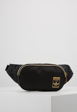 Zwarte Adidas heuptas met gouden ritsen en logo, met een voorvak en verstelbare zijbanden, tentoongesteld op een wit voetstuk.
