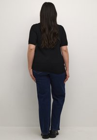 Top negro de manga corta combinado con jeans de pierna recta azul oscuro. El conjunto tiene un ajuste relajado y una textura suave, con calzado negro.