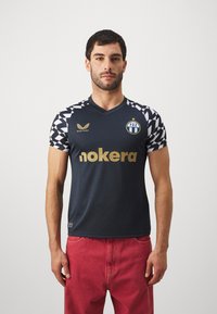Marineblaue Fußballtrikots mit kurzen Ärmeln, die ein Schachbrettmuster auf den Schultern aufweisen, goldenen "nokera"-Schriftzug und das FCZ-Logo.