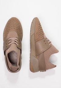 Zapatos deportivos marrones que combinan tela texturizada con detalles perforados, con suela de goma y un diseño único con recortes.