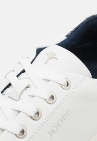 Weiße Ledersneaker mit navyblauem Innenfutter, ausgestattet mit silbernen Ösen und einem kleinen geprägten Logo-Detail an der Seite. Strukturierte Schnürsenkel sind enthalten.