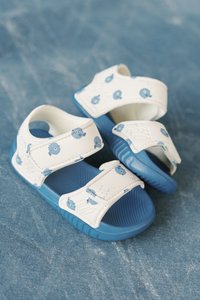 Λευκά σανδάλια με μπλε λεπτομέρειες και σχέδια μικρών ψαριών· εξοπλισμένα με δύο ρυθμιζόμενους ιμάντες βέλκρο και υφή στις σόλες για καλύτερη πρόσφυση.