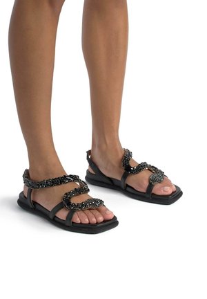 Sandali piatti neri con design intrecciato e decorazioni in perline, finitura liscia e punta aperta, adatti per un abbigliamento casual.