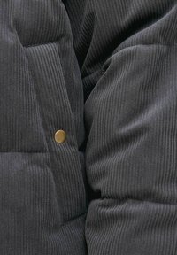 Close-up van zwarte geribbelde stof met doorgestikte quilten en een enkele kleine ronde metalen knoopdetail.