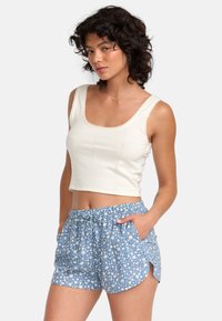 White cropped tank top with lace trim paired with blue shorts featuring a floral pattern and side pockets, made of lightweight fabric.