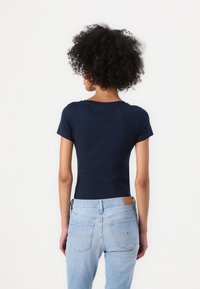 Mørkeblå kortermet t-skjorte med rund halsringning, tettsittende design og glatt tekstur, kombinert med lyseblå jeans med baklommer.