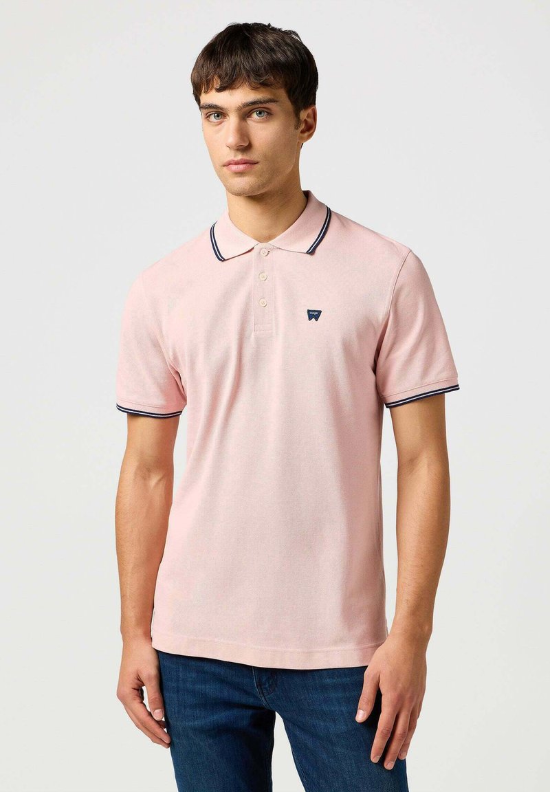 Jasnoróżowa koszulka polo z kołnierzykiem, dwoma guzikami i granatowymi wykończeniami na kołnierzyku oraz rękawach, z małym logo na klatce piersiowej.
