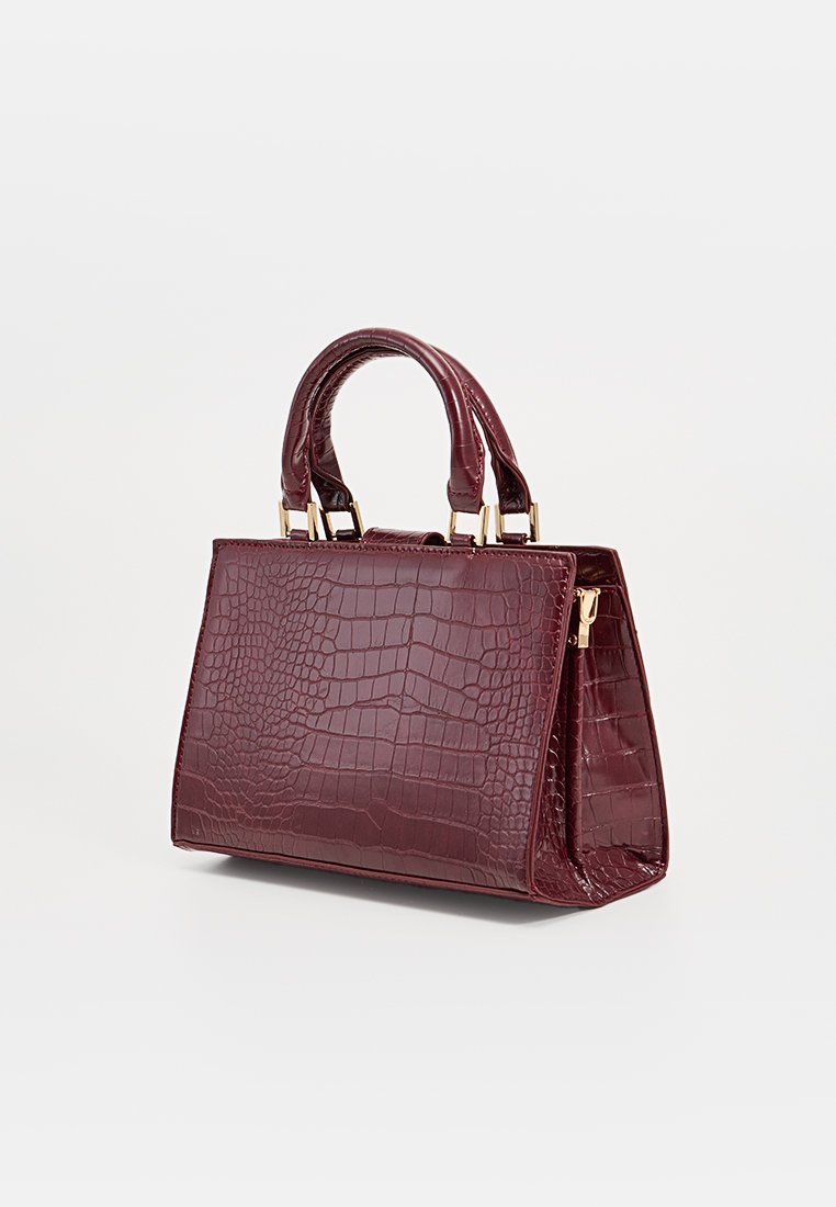 Sac à main en cuir crocodile bordeaux avec une forme structurée, deux poignées supérieures et des accents en métal doré. Compartiment principal zippé.