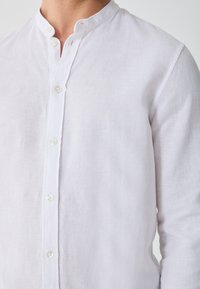 Witte linnen blouse met een mandarinakraag, knoopsluiting aan de voorkant en een subtiele textuur, met een losvallende pasvorm en lange mouwen.