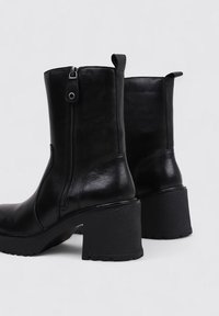 Black leather ankle boots with a chunky heel, side zipper detail, and pull tab. Smooth texture with a rounded toe and sturdy sole.