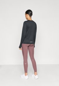 Haut de sport noir à manches longues avec col rond et coupe ajustée. Leggings bordeaux avec un motif subtil près des chevilles. Baskets blanches.