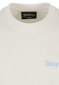 Hvid bomulds-t-shirt med rund hals, udstyret med lys blå broderet tekst "Dropsize" på venstre side og et sort mærke i nakken.