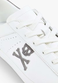 Weiße Ledersneaker mit grauem Totenkopf- und Kreuzbones-Design. Verfügt über perforierte Details und flache weiße Schnürsenkel. Glatte Textur und niedriges Profil.