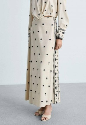 Cream long skirt with black palm tree prints and decorative side trim. Made of lightweight fabric, featuring a flowing design and smooth texture.