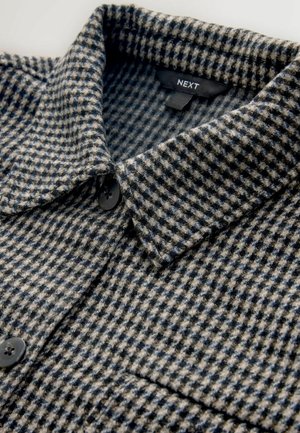 Button-up-Hemd im karierten Muster, das Grautöne, Beige und Marineblau umfasst. Das Material wirkt strukturiert mit einem ausgeprägten Kragen und einem einzelnen Knopf.