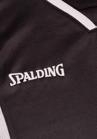 Zwart gestructureerd stof met een prominent weergegeven wit "Spalding" logo. Het ontwerp heeft een contrasterende witte rand langs de randen.