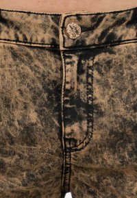 Shorts in denim marrone con un lavaggio vintage e motivi di schiuma nera, chiusura con bottone in metallo e dettagli di cucitura a vista.