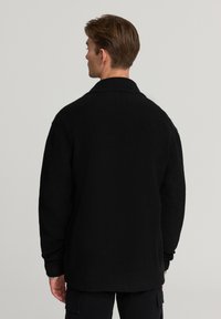 Cardigan nero a maglia con colletto a scialle e polsini a costine, caratterizzato da una vestibilità ampia e una consistenza morbida, progettato per il comfort.