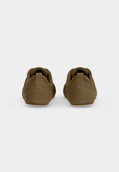Paire de chaussures marron en suède à enfiler, vues de dos, avec des languettes au talon et des semelles en caoutchouc plates sur un fond uni.