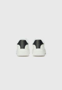 White sneakers with black leather accents, featuring a smooth texture, rounded shape, and a thick rubber sole. Subtle branding on the heel.