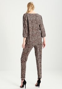 Leopardprint outfit med en løs top med trekvart ærmer og matchende tapered bukser. Materialet virker glat og let.