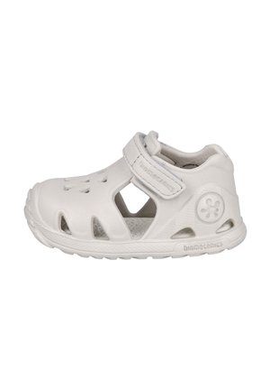 Sandalia blanca para niños con puntera cerrada, cierre de velcro, recortes laterales, suela texturizada y detalles del logo en relieve.