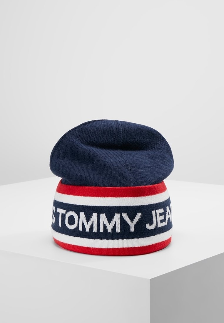 Bonnet tricoté bleu marine avec des rayures rouges et blanches, avec le texte "TOMMY JEANS" en blanc sur la bande rayée.