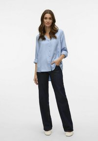 Svetlo modra srajca s kratkimi rokavi, kombinirana z temno denim kohešami. Srajca ima V-izrez in sproščen kroj.