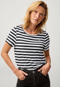Zwart-wit gestreepte t-shirt met korte mouwen en een ronde hals, gedragen met hoge zwarte jeans. Zachte stoftextuur.