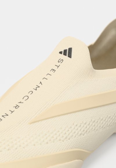 Close-up van beige Adidas Stella McCartney instapsneaker met gebreide textuur en verhoogde zijstreepdetails.