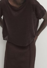 Top leggero e strutturato di colore marrone scuro, con una vestibilità ampia, maniche corte e scollatura rotonda, abbinato a una gonna aderente coordinata.