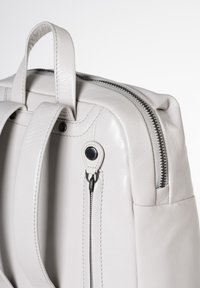 Zaino in pelle grigio chiaro con doppio manico superiore, chiusura con zip e cuciture dettagliate. Presenta un accento nero sul tirante della zip.