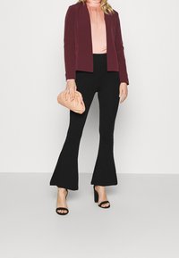 Burgundy skräddarsydd kavaj, ljusrosa plisserad topp, svarta utsvängda byxor, svarta öppna klackar och en mjuk persikofärgad kuvertväska.