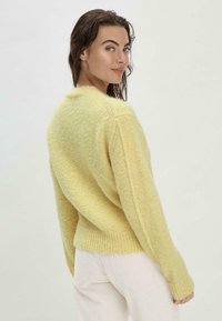 Pull en maille jaune avec une finition texturée, ourlet côtelé et manches longues. Matière douce, coupe décontractée, vue arrière visible.