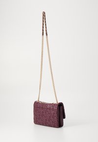 Ljubičasta kožna torba s reljefnim brendom, kviltanim uzorkom i zlatnom lančanicom. Kompaktnog pravokutnog oblika s preklopom.