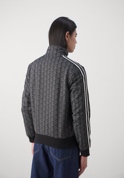 Veste noire à motifs avec un col montant, dotée de bandes blanches sur les côtés et d'un ourlet et de poignets côtelés, fabriquée dans un matériau texturé.