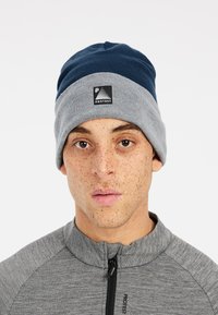Beanie in blu navy e grigio, realizzato in morbido materiale lavorato a maglia. Presenta un bordo ripiegato e un'etichetta con il logo sul davanti. Design elegante con tessuto testurizzato.