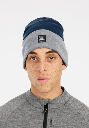 Beanie in navy blue and gray, made of soft knit material. Features a folded cuff and a logo patch on the front. Sleek design with textured fabric.