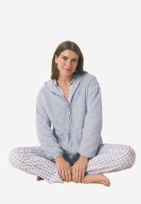 Hellblauer Fleece-Reißverschluss-Hoodie mit Taschen, kombiniert mit karierter Schlafanzughose in Blau und Weiß, getragen von einem sitzenden Modell.