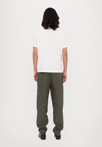 White cotton T-shirt with short sleeves, paired with olive green textured pants featuring a geometric pattern. View from the back.