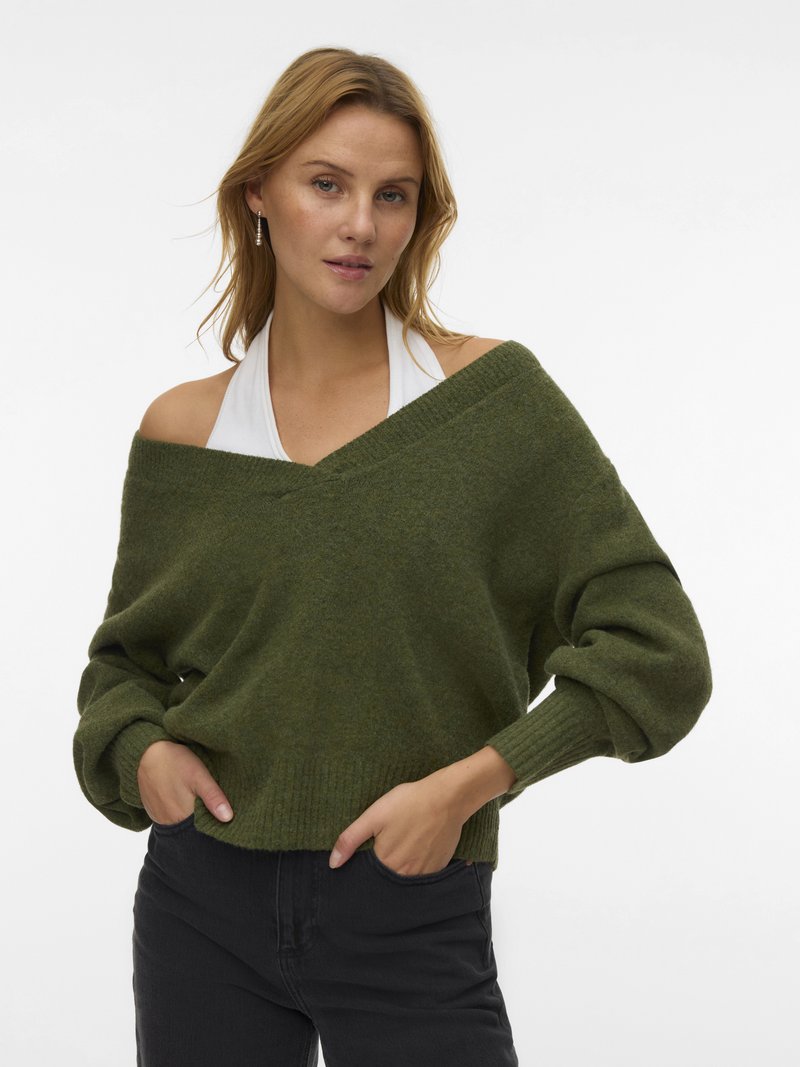 Green oversized sweater in soft knit, featuring off-shoulder design, ribbed cuffs, and a cropped hem. Paired with black pants.
