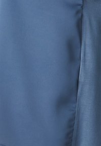 Tissu bleu clair, texture lisse, finition légèrement brillante, design ajusté avec des bords nets, idéal pour une tenue décontractée ou formelle.