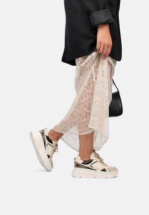 Jupe en dentelle avec un design fluide en blanc cassé, associée à des baskets beiges épaisses avec des accents noirs et des détails texturés.