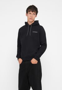Black cotton hoodie with a drawstring hood, ribbed cuffs, and hem. Features a small logo on the chest. Worn with black jeans.