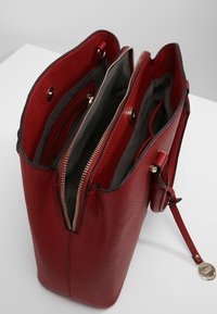 Röd texturerad läderhandväska med två dragkedjeavdelningar, grått tygfoder och detaljer i guldfärg.