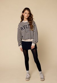 Gestreepte pullover in marineblauw en crème, met gedurfde letters. Gecombineerd met een marineblauwe rok, zwarte leggings en grijze sneakers.