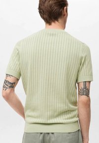Pletený svetr v světle zelené barvě s vertikálními pruhy, krátkými rukávy a žebrovaným lemem u výstřihu a na spodním okraji. Textura je hladká.